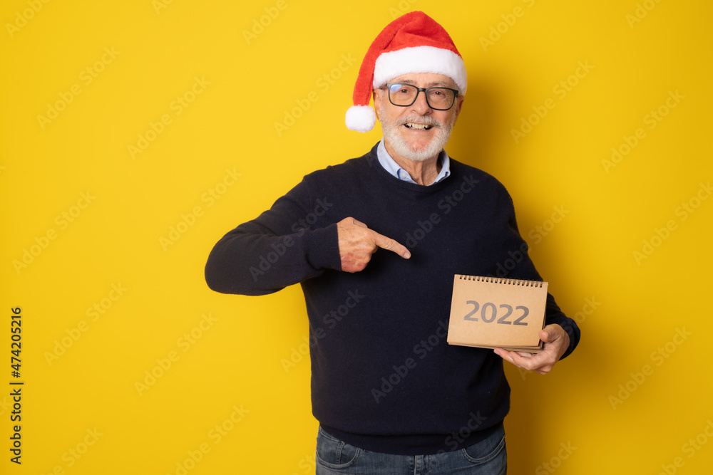 Senior smiling man wearing santa hat showing calendar isolated over yellow background. Senior smiling man wearing santa hat showing calendar isolated over yellow background.