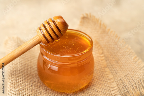 Golden organic honey in a jar with a wooden stick closeup. Concept of healthy nutrition organic food. Background for beekeepers for honey products