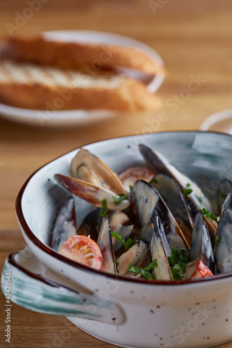 mussels with sauce in plate and grilled bread on wooden table close up. restaurant concept