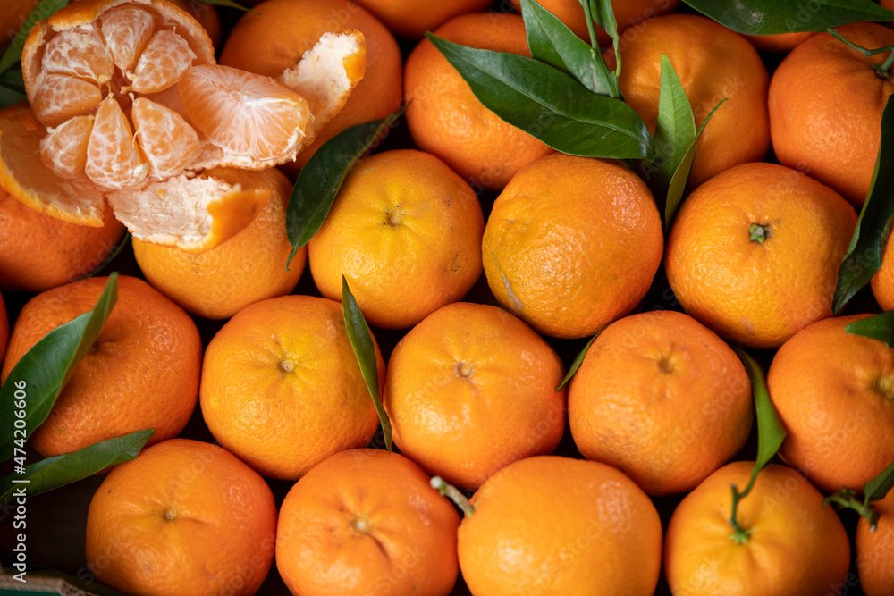 background of natural fresh tangerine with green leaves and one tangerine peeled from above