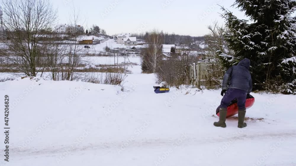 Tubing. Father pushes tube with son and he is sliding down the snow hill. Outdoor winter fun. Family leisure activity. Seasonal entertainment. Nature background. Big snowy field. Little boy and man.