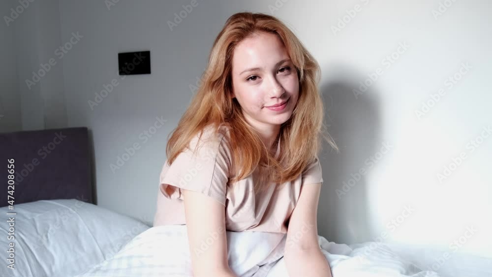 woman with positive feelings sitting on bed in pajamas and smiling at camera