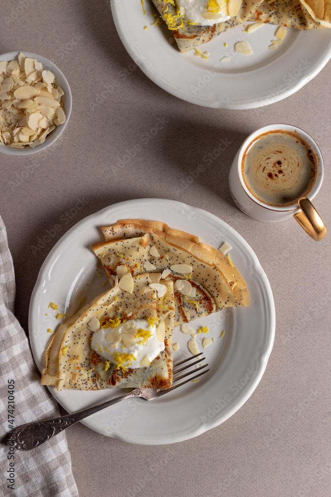 Crepes, thin pancakes with poppy seeds, lemon and sour cream on brown background. Healthy breakfast in sunny morning . Crepes, thin pancakes with poppy seeds, lemon and sour cream on brown background. Healthy breakfast in sunny morning .