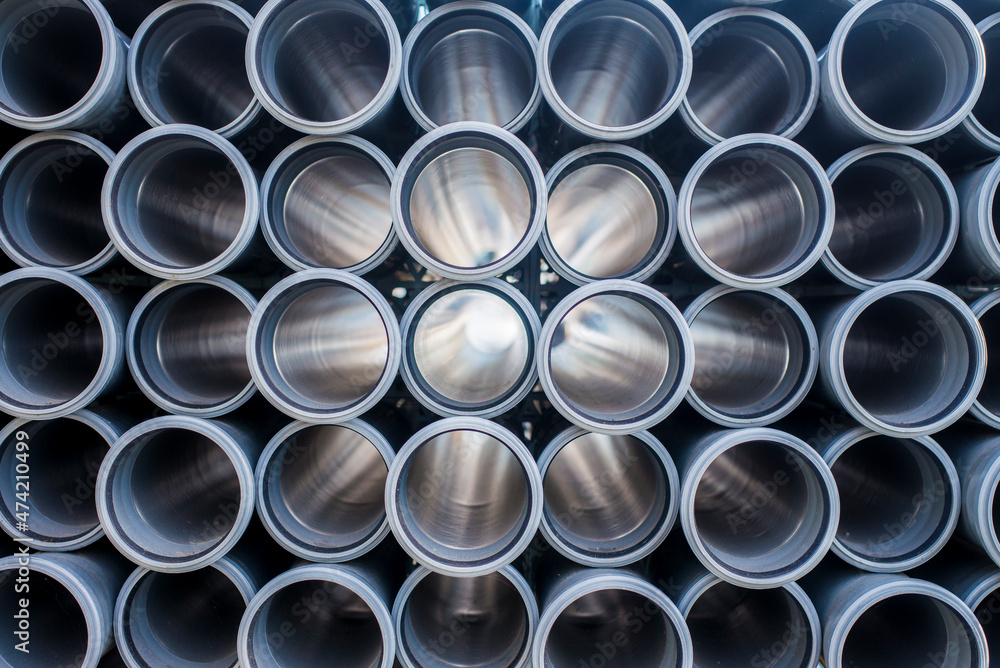 Background of grey plastic sewage pipes used at the building site. Texture and pattern of plastic drainage pipe. Light through tubes.