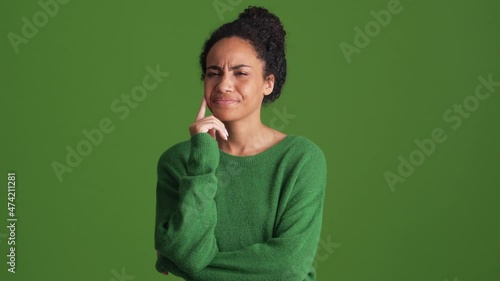 Displeased African woman in green shirt giving negative answer in the green studio photo