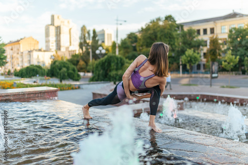 Beautiful girl in sportswear doing yoga poses on the sunset near  the fountain in the park , balance, fitness, stretching and relaxation. © Oleh