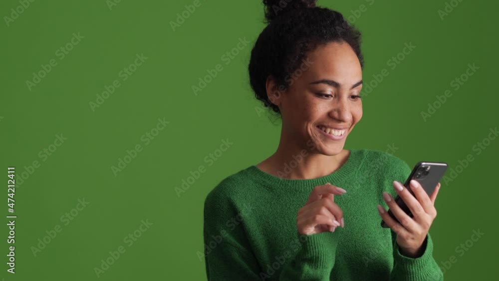 Positive African woman in green shirt flipping tape by phone in the green studio Positive African woman in green shirt flipping tape by phone in the green studio