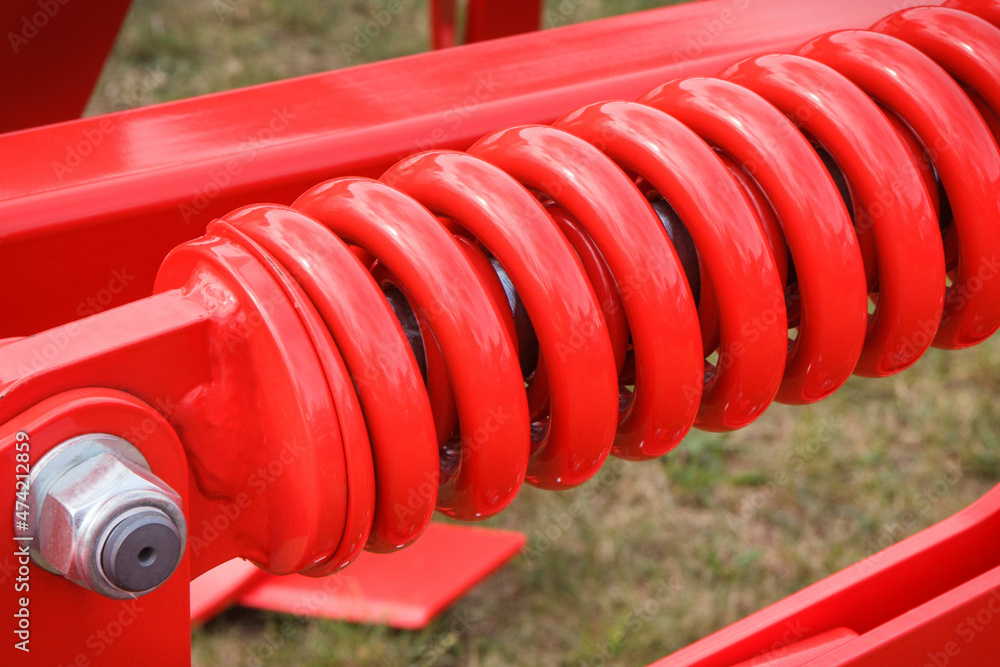 Big and hard red steel spring as part and detail of industrial or agricultural machine Big and hard red steel spring as part and detail of industrial or agricultural machine