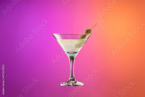 Cocktail glass with dry martini with olives isolated over gradient purple and orange color background in neon.