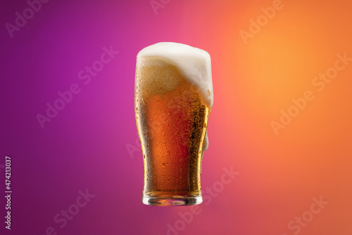Full glass of frothy light lager beer isolated over gradient purple and orange color background in neon. Concept of alcohol, drinks and festivals.