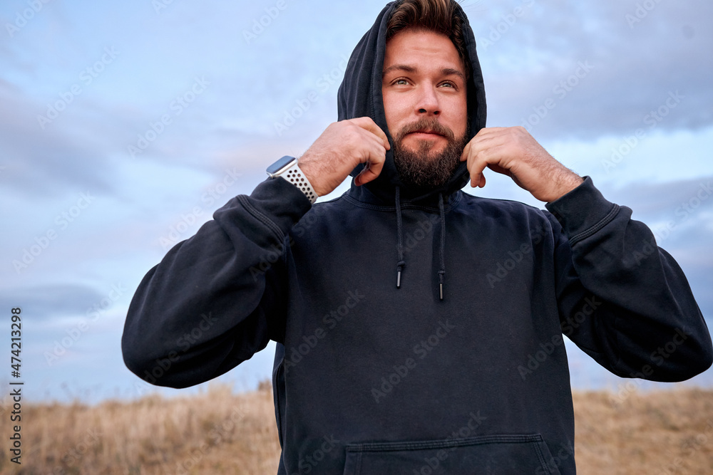 Handsome guy wearing hoodie hood, preparing for sport, training outdoors,  looking at side in contemplation. young male. european male in black wear  outfit is engaged in healthy lifestyle Photos | Adobe Stock