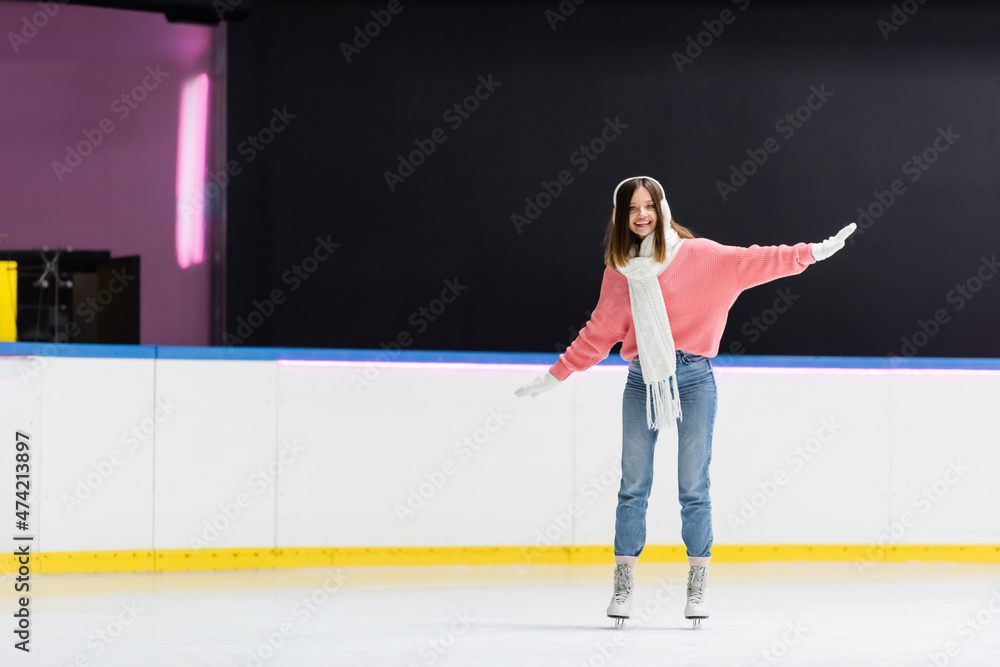 full length of smiling woman in ear muffs and winter outfit skating on ice rink. full length of smiling woman in ear muffs and winter outfit skating on ice rink.