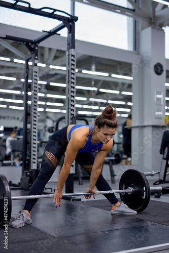 Fit strong woman performing doing deadlift exercise with weight bar in gym. Caucasian slim muscular lady in sportswear is engaged in bodybuilding. Sports concept, fat burning and a healthy lifestyle.