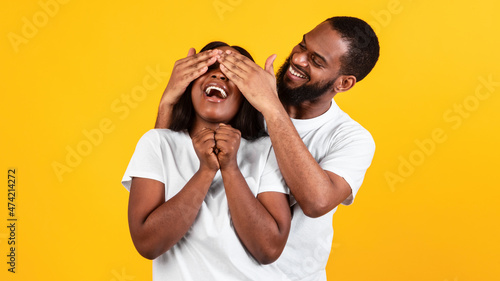 Happy black man making surprise for his woman, covering eyes