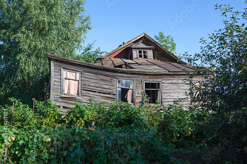 Old abandoned rustic wooden house is surrounded by the greenery of cherry orchard. Rural area. Crumbling building