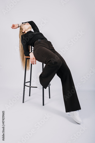 Full length studio portrait of exciting young woman fashion designer, stylist. Fashionable stylish blonde long hair girl in casual style cloth playing with chair
