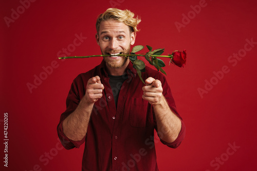 White man pointing fingers at camera while holding rose in his mouth photo