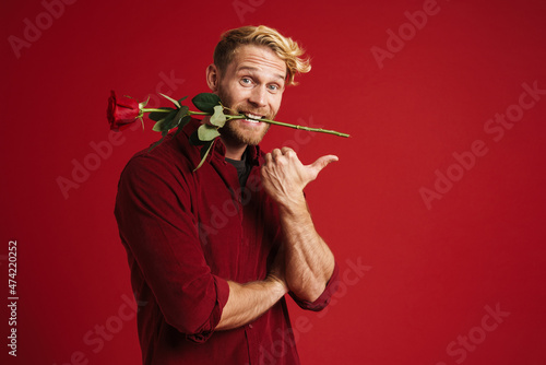 White man pointing finger aside while holding rose in his mouth photo