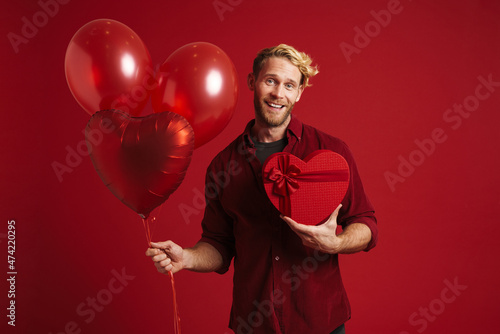 White man smiling while posing with balloons and heart gift box © Drobot Dean