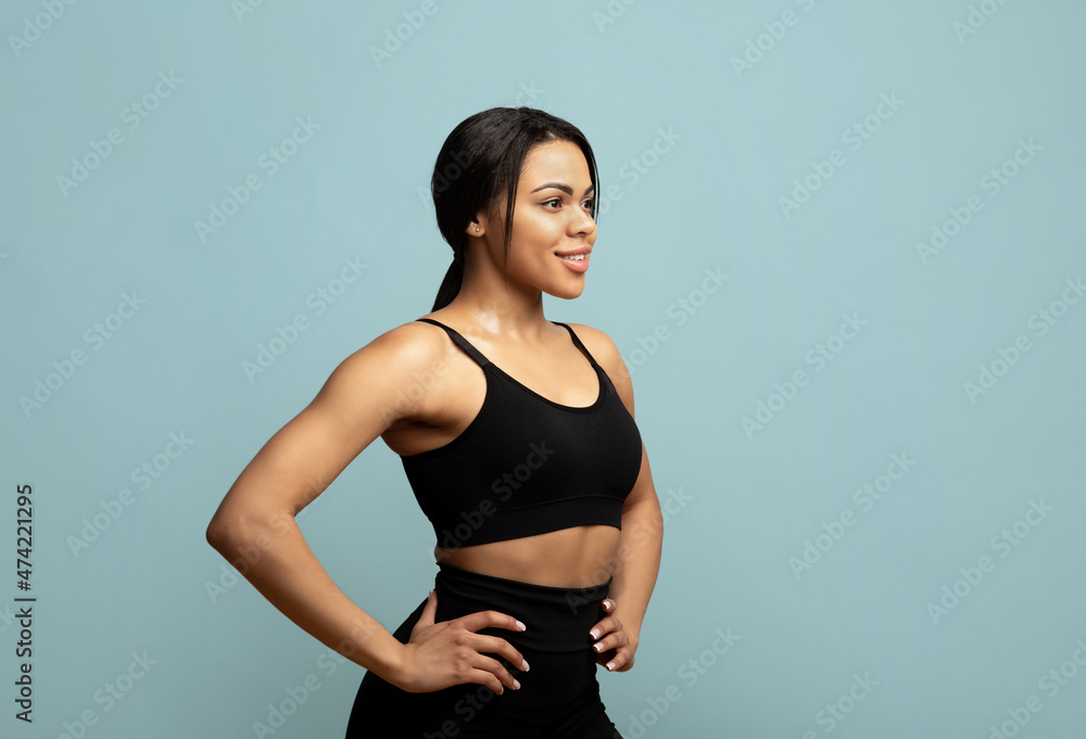 Keep fit. African american woman in sportswear posing and looking aside at free space on blue background, studio shot Keep fit. African american woman in sportswear posing and looking aside at free space on blue background, studio shot