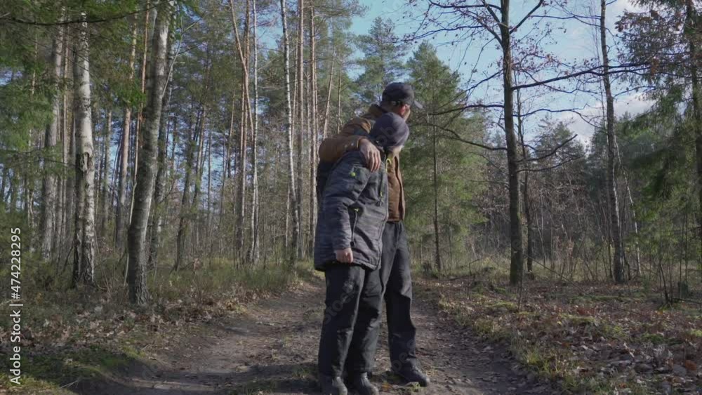 Teen boy with dad wearing casual clothing walking on forest trail. Tourism and hiking concept. Teen boy with dad wearing casual clothing walking on forest trail. Tourism and hiking concept.