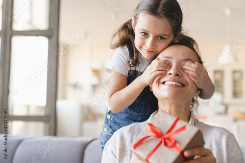 Surprise for mother. Little caucasian daughter girl giving birthday Christmas Mother s day present gift box to her mother  closing her eyes at home. Celebration event