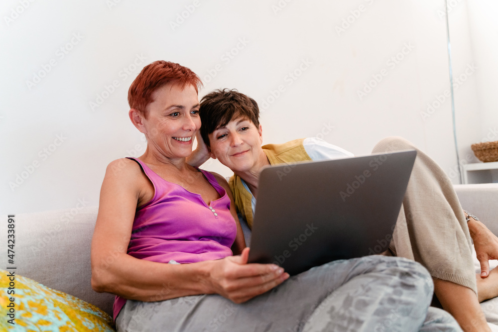 Mature lesbian couple using laptop while resting on sofa together