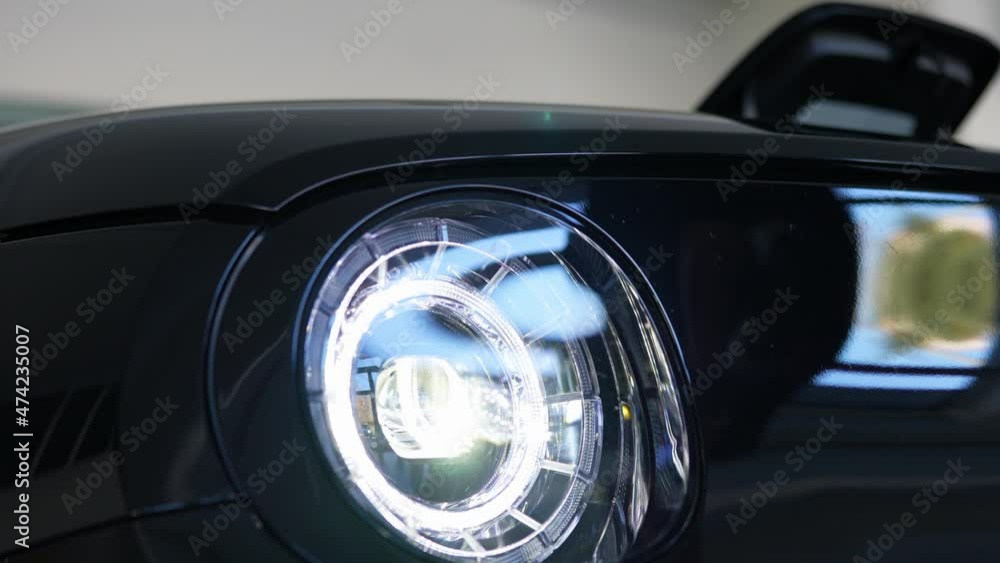 Low angle view of the headlight of a new electric car while a man charging it with a cable. Low angle view of the headlight of a new electric car while a man charging it with a cable.