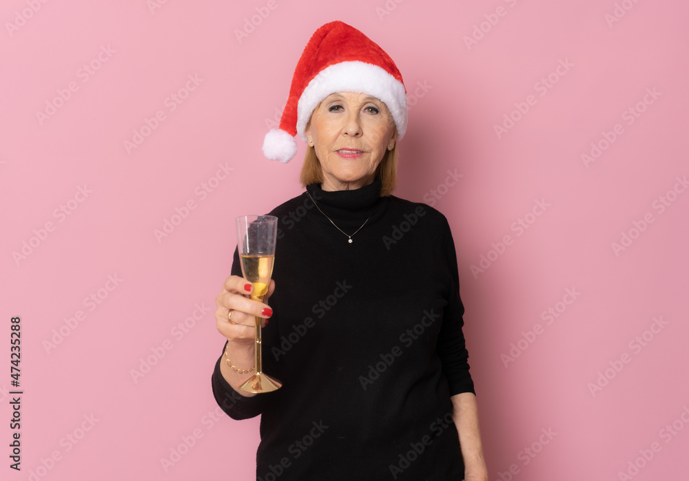 Senior woman in santa hat drinking champagne isolated over pink background Senior woman in santa hat drinking champagne isolated over pink background