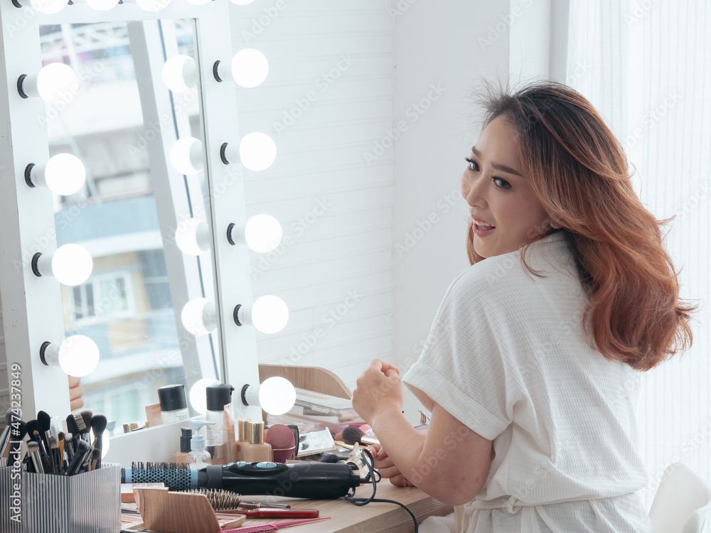 Portrait of a beautiful Asian woman doing her makeup in front of a mirror. Beautiful Asian woman applying lipstick near the cosmetic table.. Portrait of a beautiful Asian woman doing her makeup in front of a mirror. Beautiful Asian woman applying lipstick near the cosmetic table..