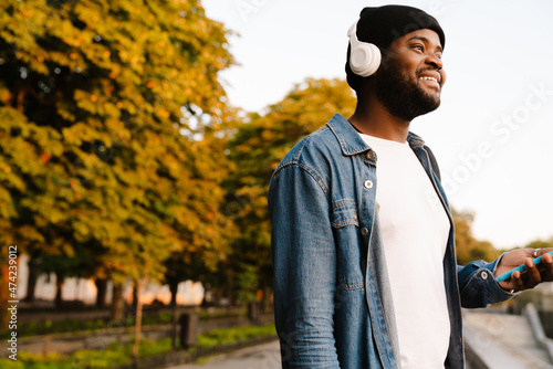 Black man in headphones using mobile phone while in autumn park