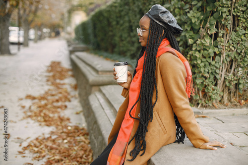 Young black woman in a coat drinking coffee outside