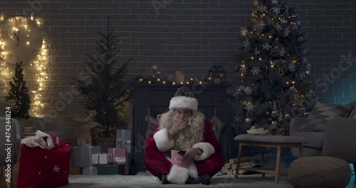 Santa Claus watching TV and eating popcorn in dark living room