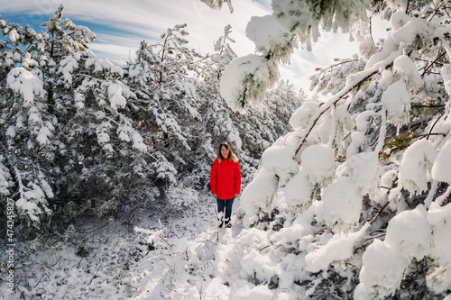 Alone woman in red jacket standing with snowy trees in winter forest. Christmas holidays