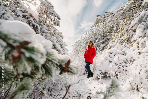 Woman in red jacket standing among snowy trees in forest. Christmas holidays