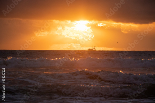 A boat sails into the sun during early morning sunrise on Daytona Beach, Florida.