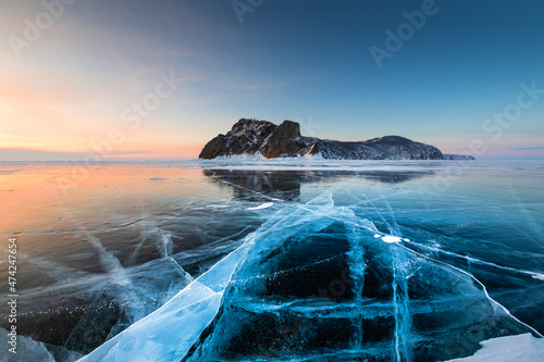 Baikal lake in winter with transparent cracked blue ice. Khoboy cape of Olkhon island, Baikal, Siberia, Russia. Beautiful winter landscape at sunrise. photo