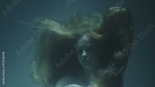 Close-up of a beautiful girl with red hair in a white dress froze under water