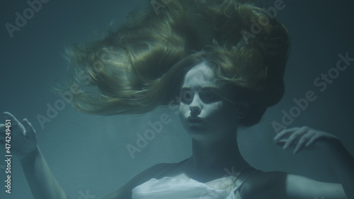 Close-up of a beautiful girl with red hair in a white dress froze under water