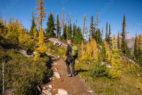 Guy hiking on a trail in the mountains with larches