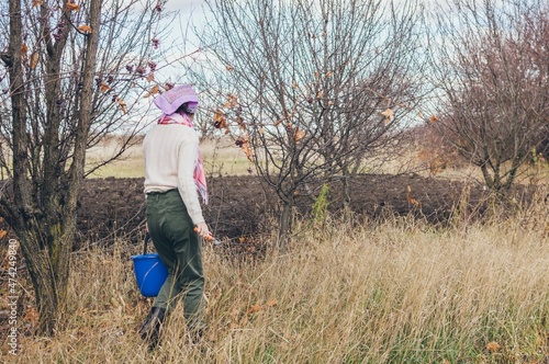 Girl with pruner and bucket in hands walks in dry grass