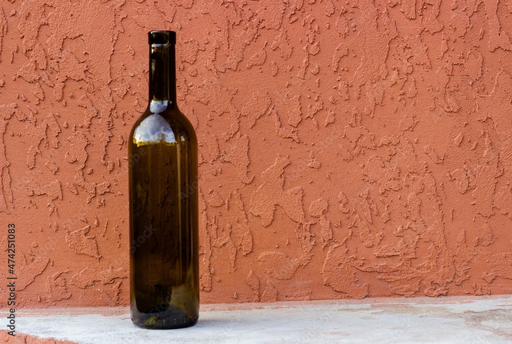 Empty 0.75 liter wine bottle against a terracotta colored concrete wall