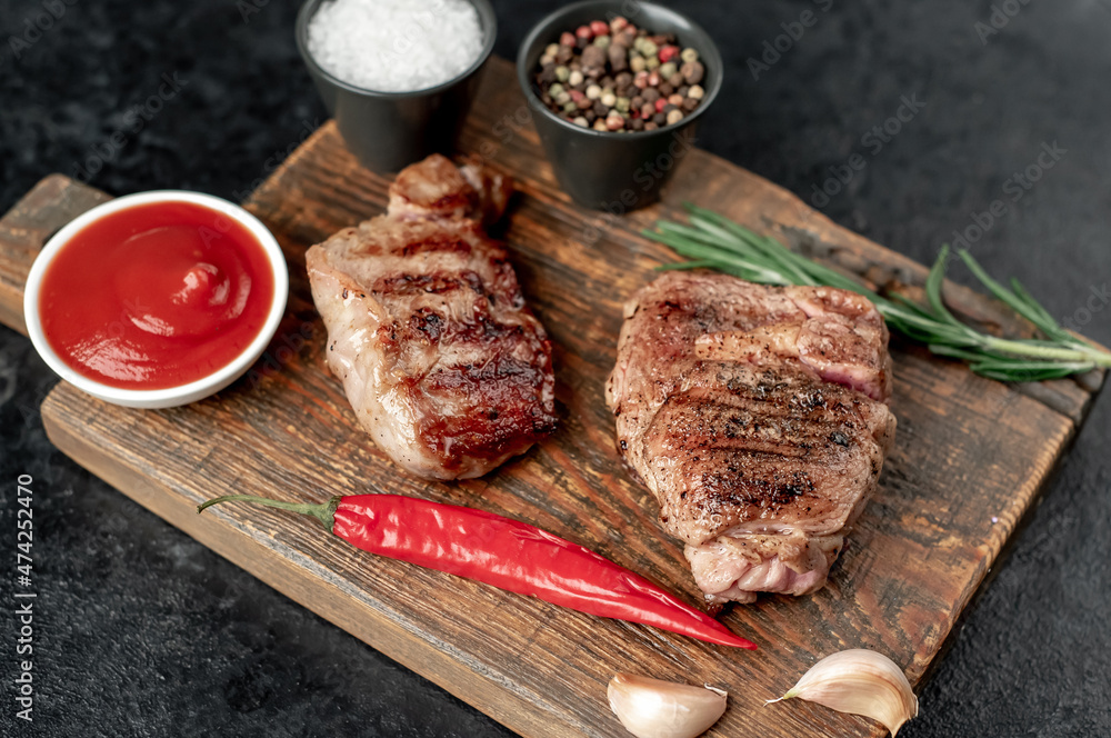 two grilled beef steaks with spices on a stone background
