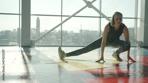 Attractive young blonde in spotswear is doing stretching exercises in light glass wall gym. Healthy lifestyle and bodycare concept. photo