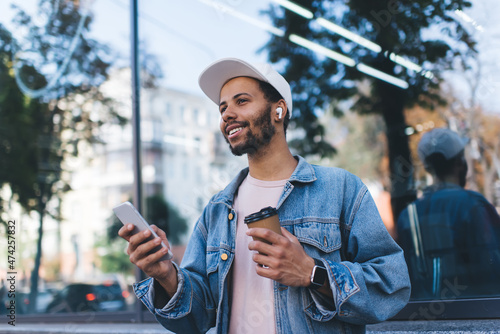 Fotografia Smiling Spanish hipster guy in bluetooth headphones enjoying positive music play