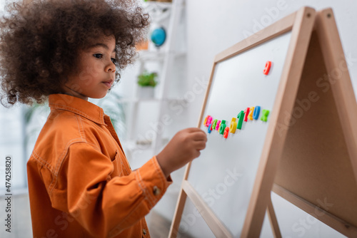 Toddler african american kid standing near magnetic board with numbers at home.
