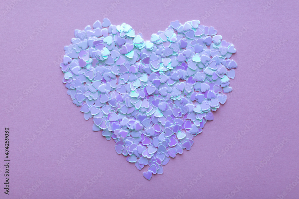 confetti sequins in the shape of hearts are laid out in a large heart on a pink background. valentine's day concept