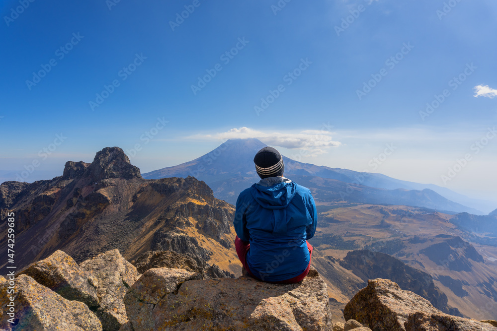 man sitting on a rock on the iztaccihuatl volcano observes the popocatepetl volcano man sitting on a rock on the iztaccihuatl volcano observes the popocatepetl volcano