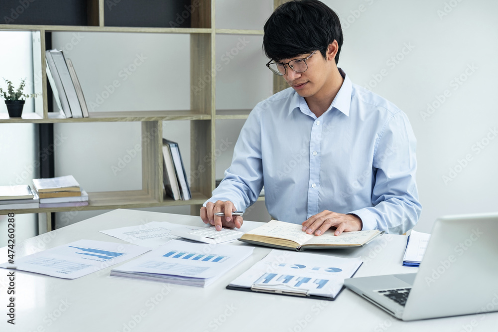 Young business man or accountant working on laptop with graph and report marketing research planning analyzing data statistics and calculator on office table Young business man or accountant working on laptop with graph and report marketing research planning analyzing data statistics and calculator on office table