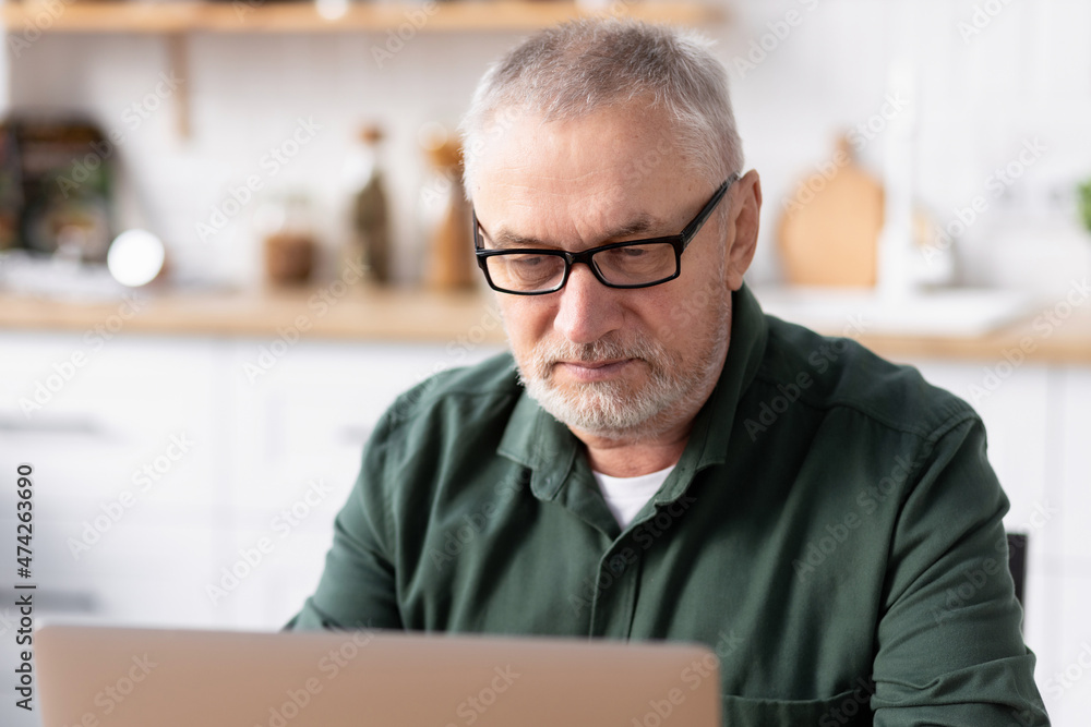 Concentrated senior man in glasses with laptop computer working at home office. Technology, remote work concept Concentrated senior man in glasses with laptop computer working at home office. Technology, remote work concept